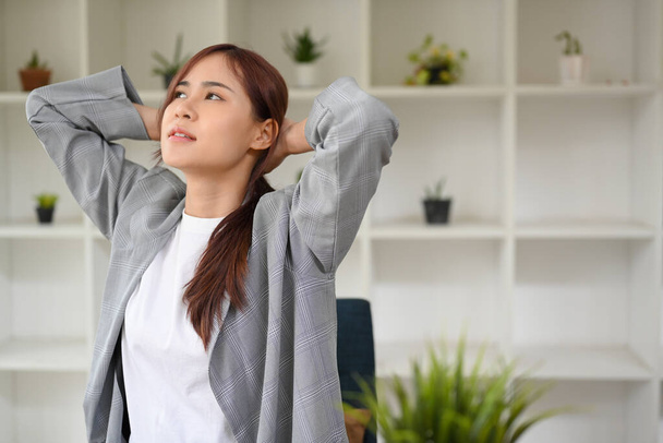 Moe jonge Aziatische zakenvrouw of vrouwelijke kantoormedewerker hand achter haar hoofd, stretching na het werk in de voorkant van haar bureau. - Foto, afbeelding