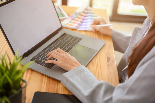 Молода азіатська жінка-графік, яка працює на своєму офісному робочому місці, використовує ноутбук для перевірки її дизайну проекту. обрізане зображення
 - Фото, зображення