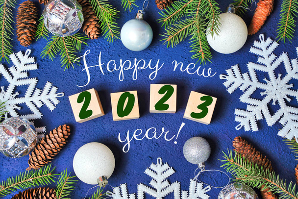Boldog új évet 2023 szöveges jel a fa kockák keret karácsonyfa ág és kúp piros háttér Hópelyhek. Kiváló minőségű fénykép - Fotó, kép