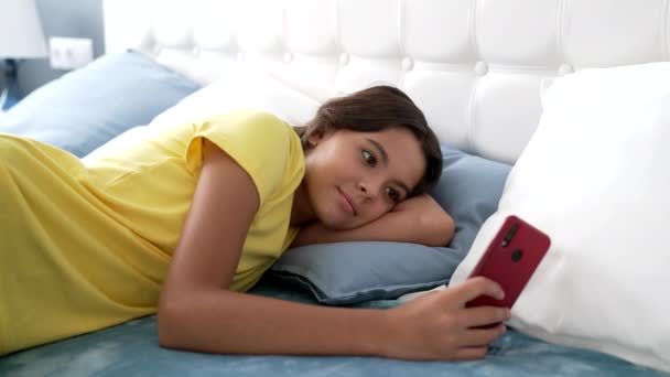 uśmiechnięte dziecko smsy na smartfonie w łóżku, blogger. - Materiał filmowy, wideo
