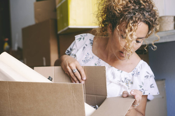 Woman at home doing boxes after a moving, mortgage loan. Renting new apartment concept. Real estate client. House pretty female people owner. New life and change, Happy lady open carton box - Photo, image