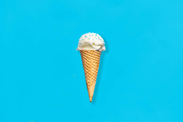 food, dessert and eating concept - close up of vanilla ice cream in waffle cone with sprinkles over blue background - Foto, afbeelding