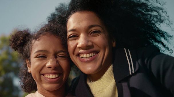Portrait smiling mom daughter in golden sunlight. Loving parent hugging child. Joyful african american family happy woman cute girl posing at clear sky. Emotional connection carefree childhood concept - Foto, afbeelding