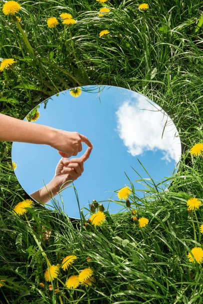 nature concept - hand touching sky reflection in round mirror on summer field - Foto, immagini