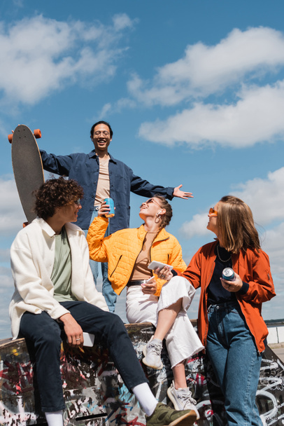 asian man with longboard standing with outstretched hands above happy friends with smartphones and soda cans - Photo, Image