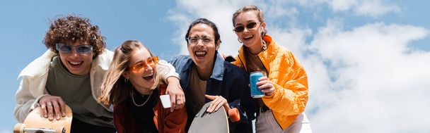 low angle view of excited multiethnic skaters laughing outdoors, banner - Foto, Bild