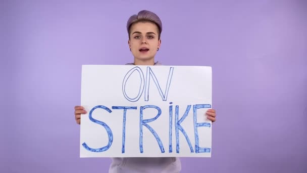 Молода доросла жінка покоління Z з коротким пофарбованим волоссям, що тримає плакат ON STRIKE, каже гасло протесту, висловлюючи занепокоєння, почуваючись стурбованою, ізольованим на фіолетовому фоні в приміщенні. Про концепцію страйку
 - Кадри, відео