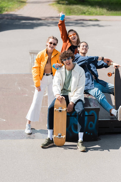 trendy and happy multiethnic skaters looking at camera outdoors - Photo, Image