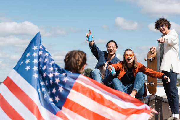 heureux amis multiethniques pointant vers femme floue avec drapeau des Etats-Unis à l'extérieur - Photo, image