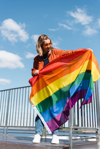 full length of young woman standing with lgbt flag near fence - Фото, изображение