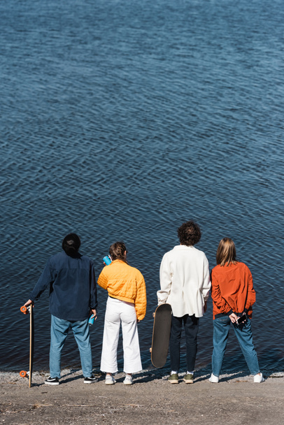vista trasera de los amigos en ropa elegante de pie en la orilla del río - Foto, Imagen