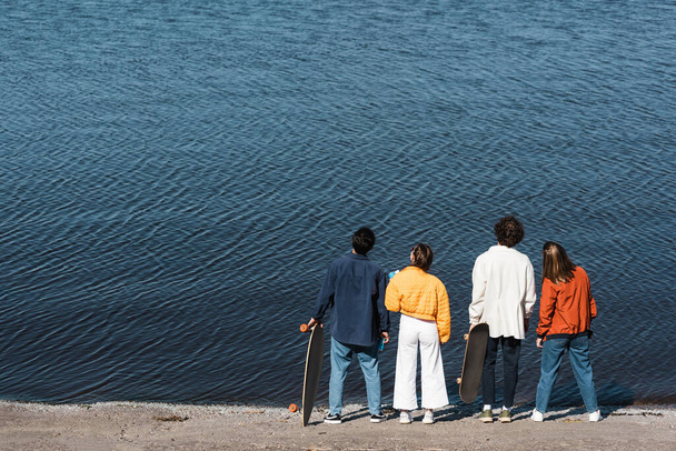 Rückansicht junger Skater in trendiger Kleidung, die am Fluss stehen  - Foto, Bild