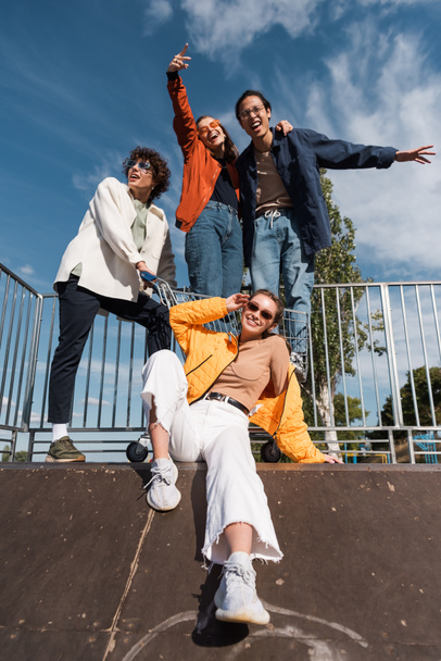 stylish woman in sunglasses near multiethnic friends on ramp in skate park - Foto, Bild