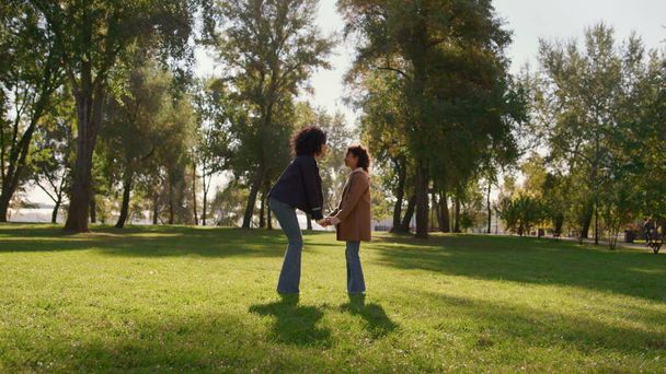 Мать держит дочь за руки нежно касаясь носов на солнечном зеленом парковом поле. Счастливая африканская американская семья, наслаждающаяся временем вместе, выражает безусловную любовь. Эмоциональная связь между матерью ребенка. - Фото, изображение