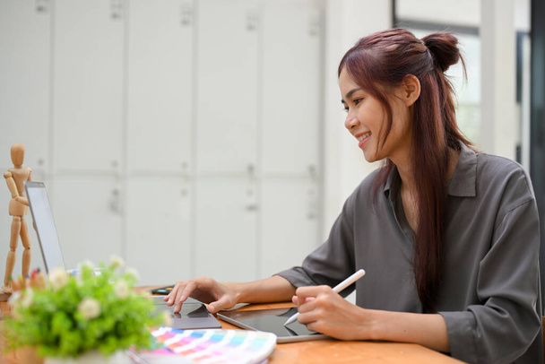 Çekici Asyalı kadın grafik tasarımcısı dizüstü bilgisayar kullanıyor, yaratıcı bir iş tasarlıyor, ofis masasında çalışıyor. - Fotoğraf, Görsel