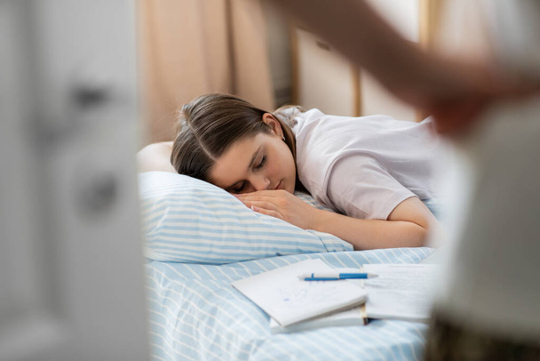 school, education and laziness concept - close up of angry parent looking at tired teenage student girl with notebooks sleeping on bed at home - Foto, immagini