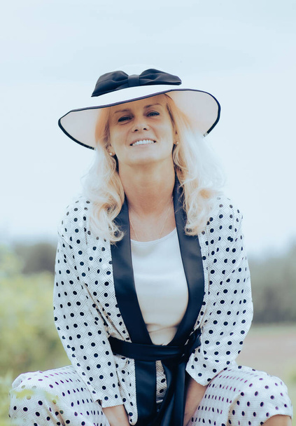 A vertical portrait of a beautiful blonde woman wearing a polka dot dress and a hat smiling - Fotografie, Obrázek