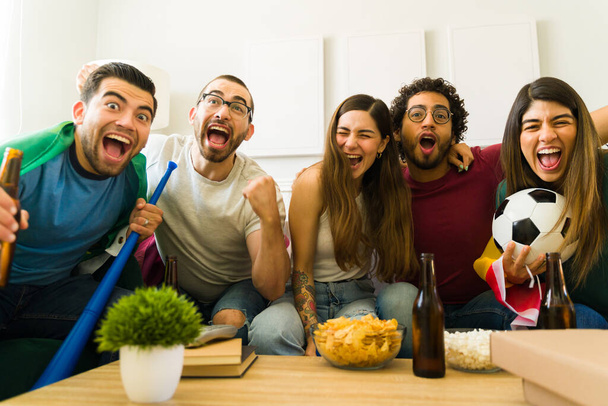 Portrait d'un groupe joyeux d'amis dans le salon criant et célébrant la victoire de leur équipe sportive  - Photo, image