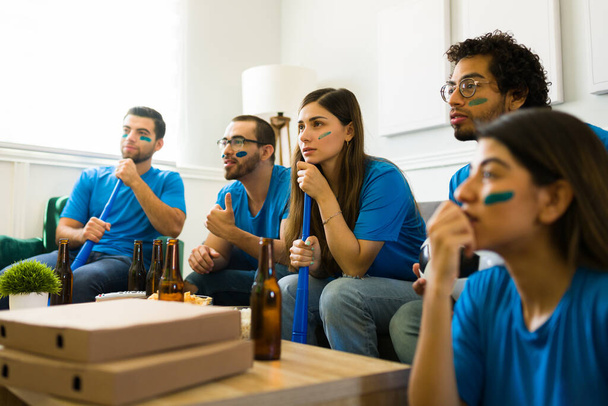 Aantrekkelijke groep vrienden ondersteunen hun nationale team en kijken naar de voetbalwedstrijd op tv en kijken bezorgd - Foto, afbeelding