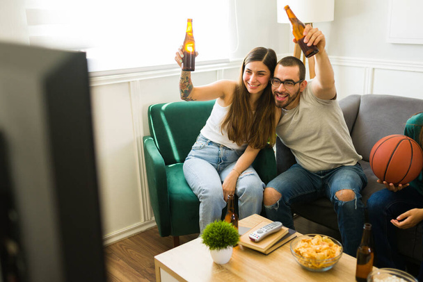 Atraktivní šťastný pár objímání a pití piva při poflakování se s přáteli v obývacím pokoji - Fotografie, Obrázek