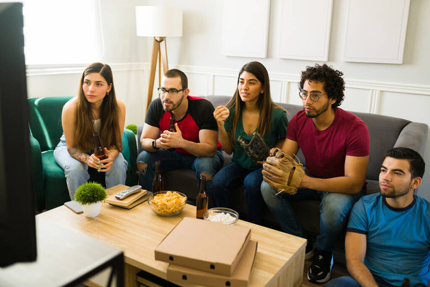 Grupo multirracial de amigos sentados en el sofá y ansiosos mientras disfrutan de un partido de béisbol en la televisión - Foto, imagen