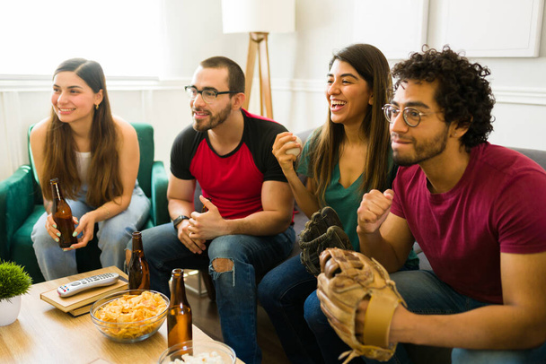 Attractive young friends smiling and laughing while watching the baseball game on tv - Photo, Image
