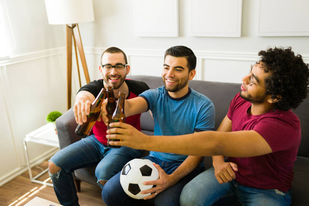 Szczęśliwi przyjaciele wznoszący toast z piwem podczas oglądania meczu sportowego w telewizji  - Zdjęcie, obraz