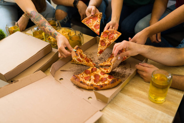 Close up of the hands of young women and men grabbing a slice of pizza while hanging out  - Фото, зображення