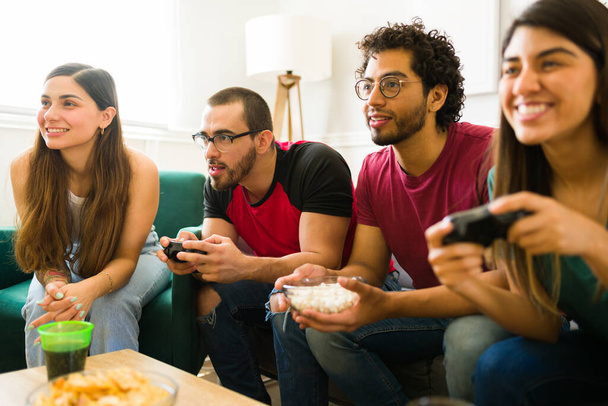 Two couples sitting on the sofa and playing video games while enjoying drinks and snacks  - Photo, image