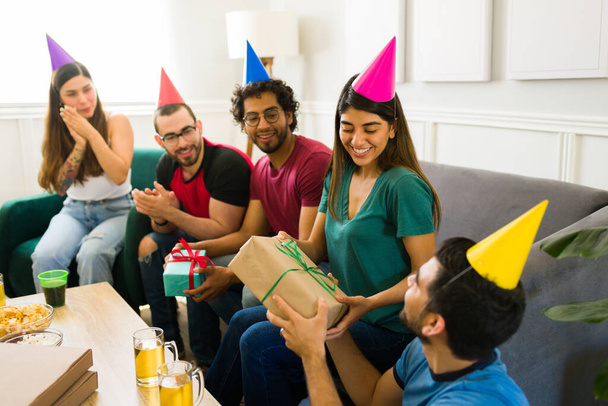 Alegre grupo de amigos en una fiesta de cumpleaños en casa dando regalos a una joven feliz  - Foto, imagen