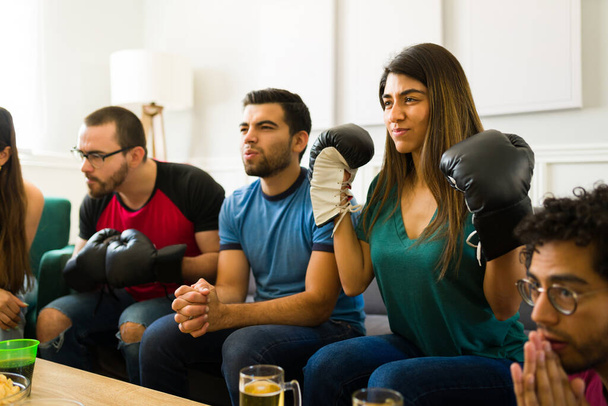 Atrakcyjna Latynoska kobieta i jej przyjaciele oglądają wspólnie zawodową walkę bokserską w telewizji - Zdjęcie, obraz