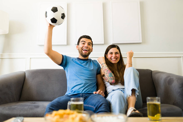 Jeune couple excité regardant la télévision et criant tout en acclamant pour leur victoire de l'équipe nationale de football  - Photo, image