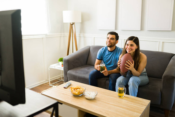 Fani sportu uśmiechnięci podczas oglądania meczu piłki nożnej w telewizji, ciesząc się piwem i przekąskami  - Zdjęcie, obraz