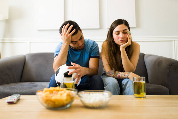 Smutna młoda kobieta i mężczyzna i fani sportu czują się rozczarowani po obejrzeniu meczu piłki nożnej w telewizji - Zdjęcie, obraz