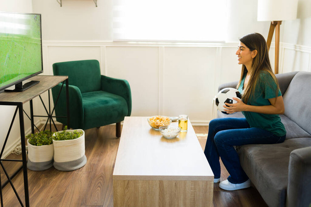 Vrouwelijke sportfan op zoek gelukkig terwijl u geniet van een kampioenschap voetbal op tv en ontspannen thuis  - Foto, afbeelding