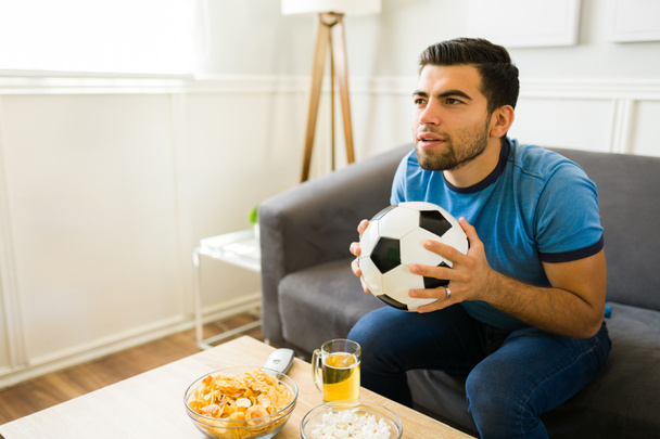Handsome young man feeling worried about the score during a soccer match on tv  - 写真・画像