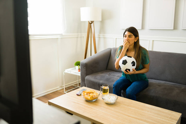 Ανήσυχη γυναίκα φίλαθλος τρώει τα νύχια της, ενώ βλέποντας την εθνική ομάδα ποδοσφαίρου παίζει ένα παιχνίδι στην τηλεόραση - Φωτογραφία, εικόνα