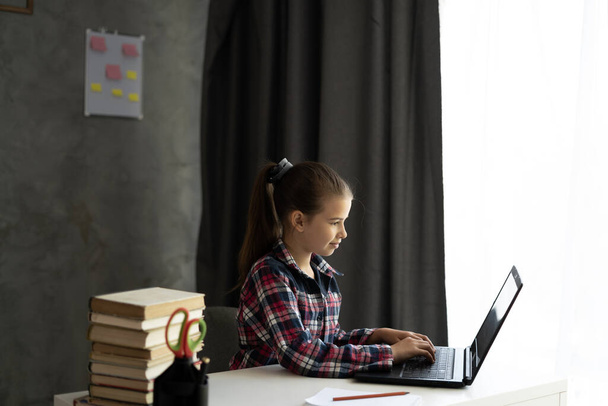 Дистанционное образование, онлайн-занятия. Прекрасная школьница, изучающая домашнюю работу во время онлайн-урока дома, самоизоляция, общение через Интернет, концепция электронного обучения - Фото, изображение