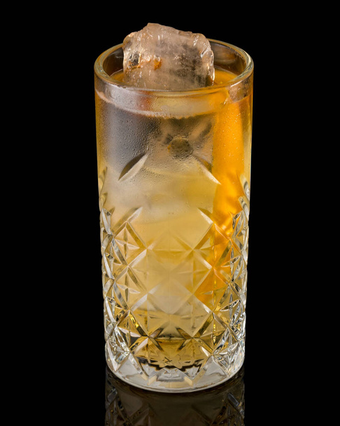 A closeup shot of a glass of cocktail with an orange slice in it over a black background - Фото, изображение