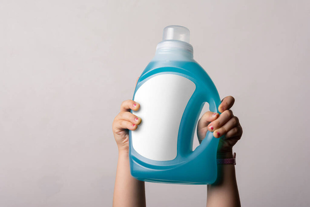 Cloth detergent liquid bottle at little girl hands in front of light gray background, editable mock-up series template ready for your design - Foto, Bild