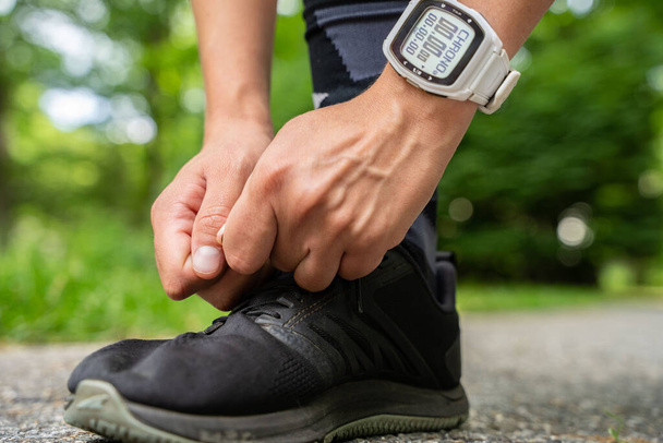 A young man with a watch on hand tying running shoes - 写真・画像