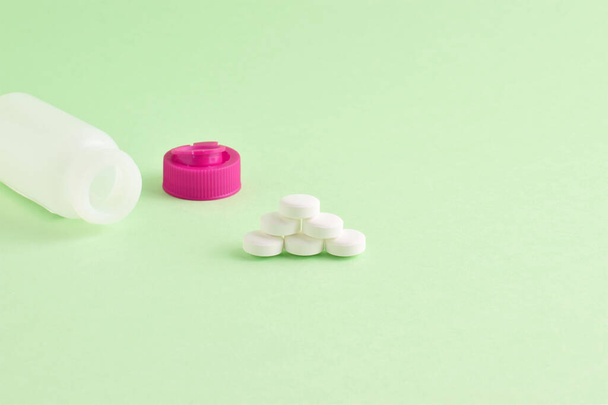 A closeup shot of the medicines. The white pills and small bottle on light green background - Zdjęcie, obraz