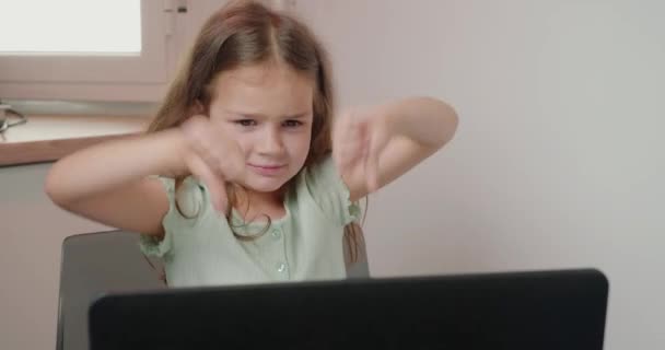 Neşeli kız ev ödevini bitirdikten sonra baş parmak hareketini gösteriyor. Tatmin olmamış küçük kız evdeki bilgisayarın yanında oturuyor. - Video, Çekim