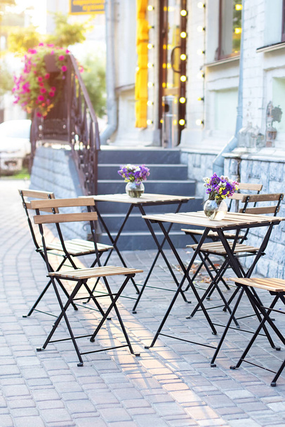 Café vazio com terraço com mesas e cadeiras. Rua exterior do restaurante. Flores em vaso na mesa. Mobiliário para café na rua na Europa no verão. Velha rua acolhedora com mesas de café - Foto, Imagem
