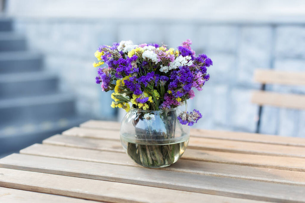Bouquet of summer flowers in glass vase on table on terrace. Fresh Field flowers in vase. Cozy home decor of patio yard. Still life. Women day or wedding concept. festive background, copy space - Valokuva, kuva
