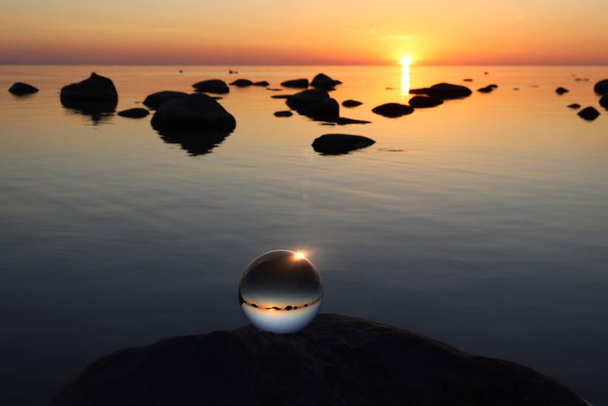 Kristallen bal op rotsachtig strand op een grote grijze granieten rots, zonsondergang reflecterende - Foto, afbeelding