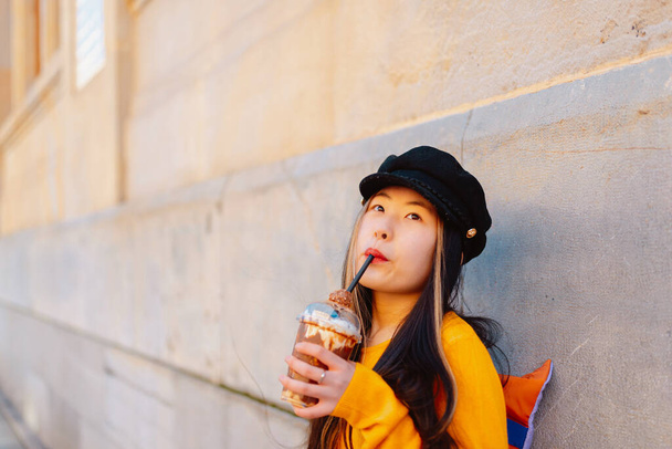 Asiática joven felizmente bebiendo un batido de chocolate en la calle mientras que turismo en una ciudad europea. - Foto, imagen