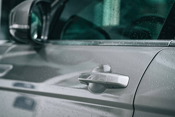 A closeup of the door handle of a modern grey car under the rain - Fotó, kép