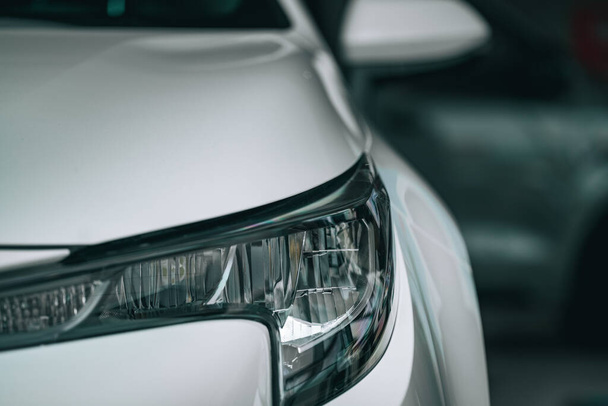 A closeup shot of the front part of a white car and the headlight with small raindrops - Фото, изображение