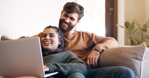 Foto de una pareja joven usando un portátil mientras se relaja en el sofá en casa. - Foto, imagen